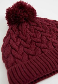 Burgunderfarbene Strickmütze mit einem strukturierten geflochtenen Muster, geripptem Saum und einem flauschigen Pompon oben. Weicher Wollmischstoff.