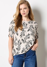 Lys beige kortærmet bluse med et trykt sort bladmønster. Stofdet ser glat ud, med en afslappet pasform og rund halsudskæring.