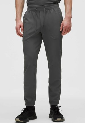Uomo che indossa pantaloni jogger grigio scuro con trama, con vita elasticizzata e coulisse, abbinati a scarpe sportive nere e calzini neri.