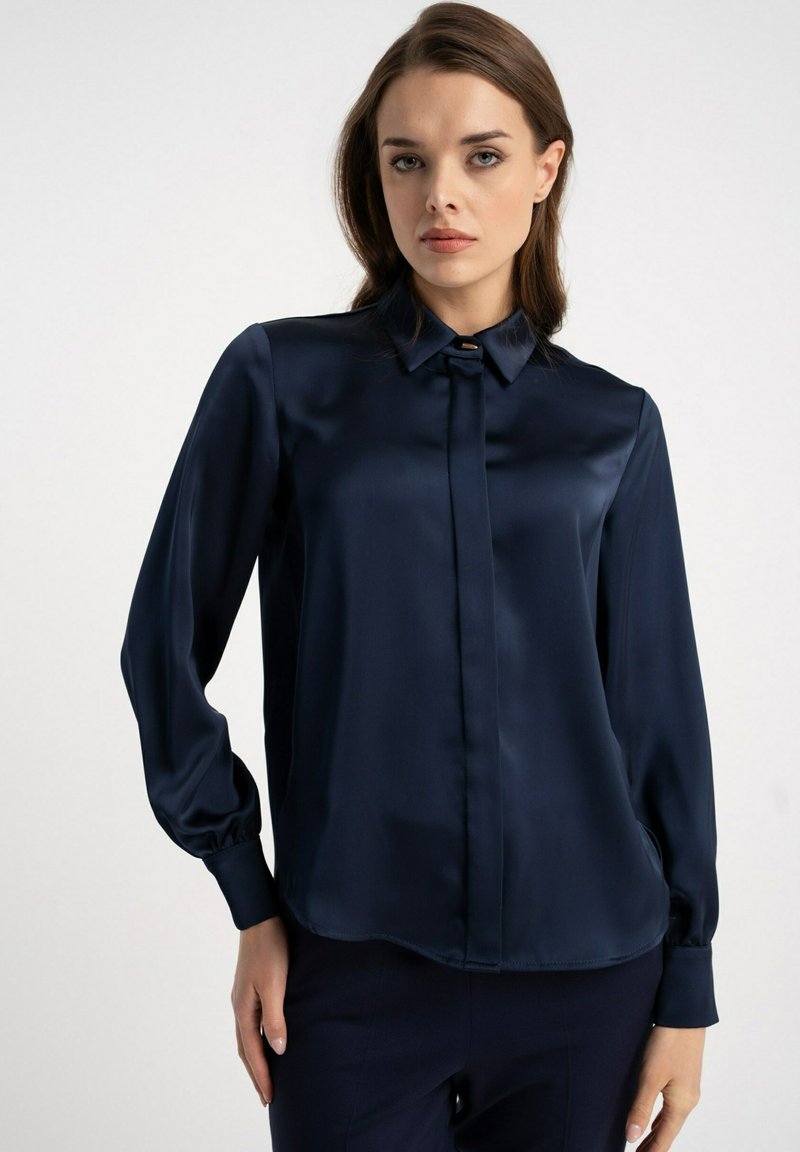 Granatowa satynowa bluzka z klasycznym kołnierzem, długimi bufkowatymi rękawami i zapięciem na guziki, o gładkiej fakturze i subtelnym połysku.