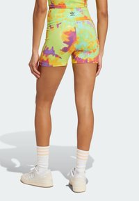 Färgglada tie-dye-shorts i neon-gul, orange och lila. Mjuk tyg med hög midja, kombinerat med vita sneakers och randiga strumpor.