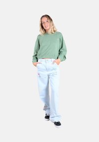 Sweatshirt vert court, jean bleu clair à large jambe avec des accents brodés et baskets en toile noires. Tissu lisse, coupe décontractée.