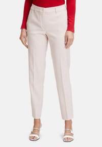 Pantaloni su misura rosa chiaro con gamba dritta, pieghe frontali e chiusura con bottone, abbinati a sandali bianchi con lacci. Finitura in tessuto liscia.