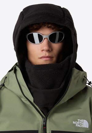 Person som har på seg svart fleece balaklava, smale svarte solbriller og grønn The North Face-jakke med frontglidelås og snor.