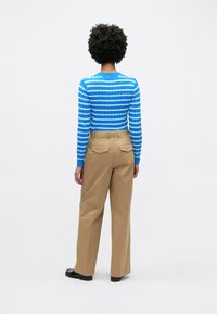 Πλεκτό π ουλόβερ με ρίγες σε μπλε και άσπρο, συνδυασμένο με μπεζ παντελόνι φαρδιάς γραμμής. Σημαντικές λεπτομέρειες περιλαμβάνουν πίσω τσέπες και υφασμάτινο ανάγλυφο μοτίβο στο πουλόβερ.