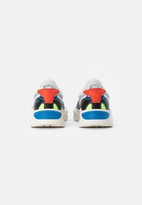 Les sneakers présentent une tige en mesh et synthétique aux couleurs blanc, bleu, noir et rouge. Parmi les accents remarquables, on note un talon texturé et des détails intérieurs vibrants.