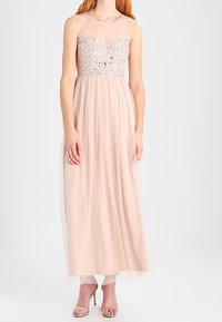 Lång, ljusrosa klänning med en genomskinlig bodice prydd med silverbroderi, som har en flödande tyllkjol och tunna axelband.