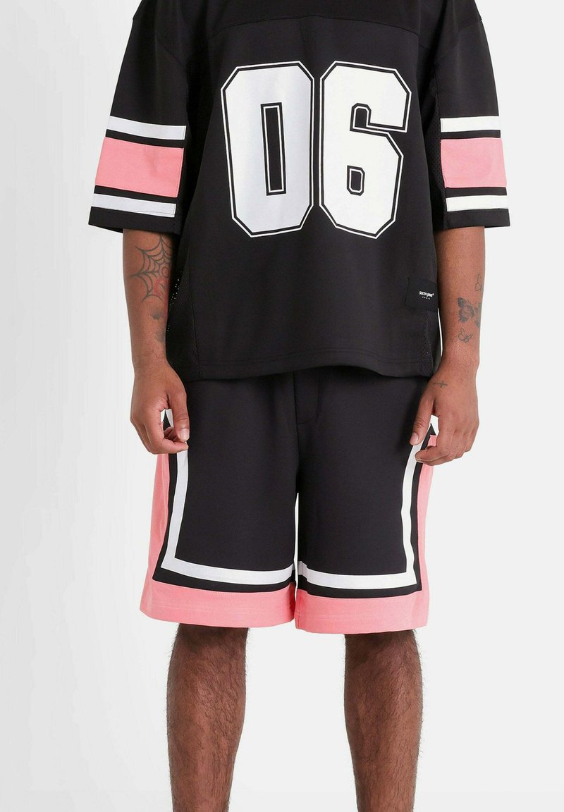 Zwarte sporttrui met witte nummer 06 en roze accenten op de mouwen, gecombineerd met zwarte shorts met roze en witte details, met een gladde textuur.