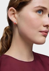 Orecchini in argento con gemme chiare e arancioni, caratterizzati da un design floreale. Il modello indossa un top bordeaux, catturato di profilo.