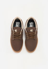 Brown canvas sneakers with beige lining, round toe, and brown laces. Features a rubber sole and a logo on the side.