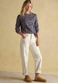 Námořnický top s květinovým vzorem a dlouhými rukávy, krémové kalhoty a hnědé pantofle. Měkké materiály s uvolněným střihem a ohrnutými manžetami.