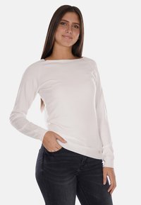 Maglione bianco a maniche lunghe con scollatura a barca, polsini e orlo a costine. Tessuto morbido, design minimal. Abbinato a jeans scuri.
