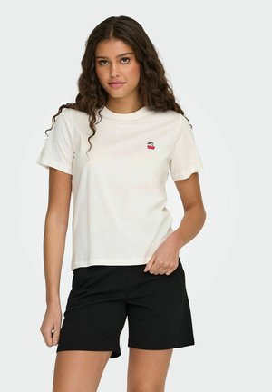 T-shirt en coton écru à manches courtes, avec une petite broderie de cerise sur la poitrine. Associé à un short noir.