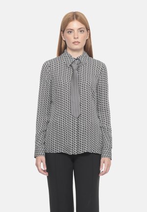 Camicia a maniche lunghe a fantasia bianca e nera con colletto e cravatta, realizzata in un tessuto morbido e con una vestibilità su misura. Indossata con pantaloni neri.
