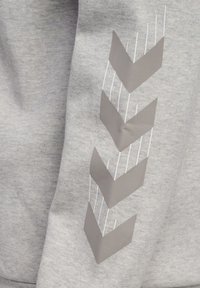 Tissu gris clair avec quatre flèches chevrons gris foncé pointant vers le bas et de fines lignes verticales blanches à côté des flèches.