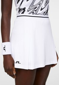 Gonna da tennis bianca con pieghe, striscia nera di accento in vita e logo vicino all'orlo. Accompagnata da un braccialetto bianco con logo.