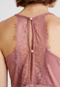 Rosa klänning med spets på ryggen, med scallopade kanter och en knappdetalj vid nacken. Mjuk textur och svängig design.