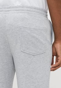 Gray sweatpants featuring a textured fabric, elastic waistband, and a single patch pocket on the right side. Smooth finish with casual design.