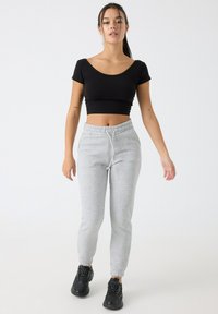 Camiseta negra corta combinada con pantalones de chándal gris claro con cintura elástica y tobillos ajustados, usados con zapatillas negras.