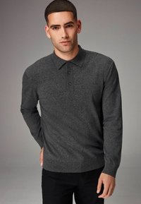 Polo de manga larga tejido en gris oscuro con cuello y tapeta de tres botones. Presenta puños y dobladillo acanalados. Textura suave, diseño ajustado.