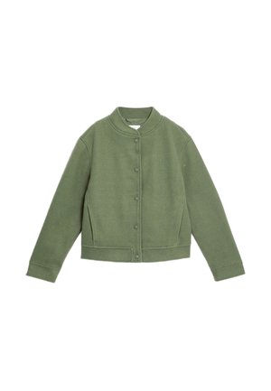 Person med flettet hår set bagfra iført en olivengrøn jakke med en hvid fleecekrave, blå viddebukser og sorte sko.