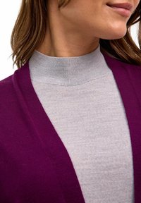 Cardigan violet sur un col roulé gris, avec une texture côtelée. Gros plan sur le design de l'encolure et du col, montrant des matériaux doux et superposés.