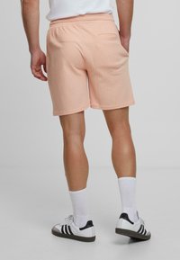Perzikkleurige fleece shorts met een gestructureerde stof, elastische tailleband en een achterzak. Gekocht met witte sokken en zwart-witte sneakers.