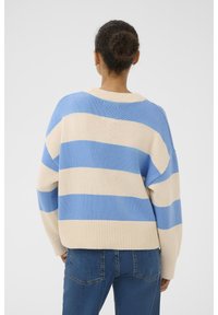 Pulover tricotat în dungi albastre și bej, cu o croială lejeră, decolteu tip barcă și tiv cu nervuri, combinat cu blugi din denim.