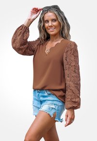 Braune Bluse mit strukturierten Spitzenärmel, gewelltem Ausschnitt und leichtem Stoff. Kombiniert mit zerrissenen Denim-Shorts für einen lässigen Look.
