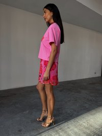 T-shirt fucsia corto con design floreale, abbinato a una mini gonna fiorata fucsia. Sandali con tacco a strappo neri e beige completano il look.