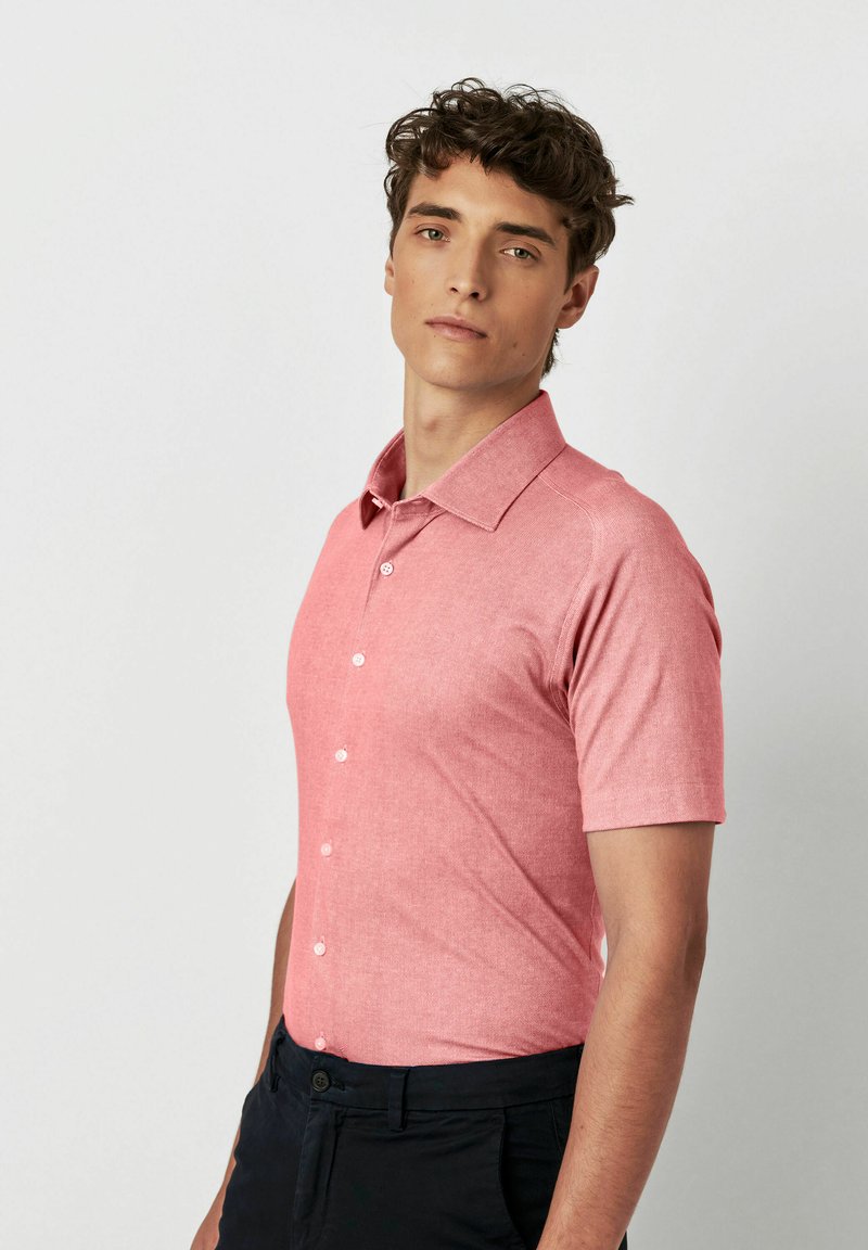 Korte mouwen polo-shirt in een lichtroze, gestructureerde stof met een kraag en knoopsluiting, gecombineerd met donkere broek.