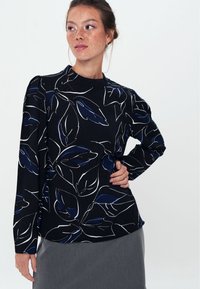 Blusa nera a maniche lunghe con pattern a foglie bianche e blu, scollatura rotonda, tessuto testurizzato e leggero volume alle cuciture delle spalle.
