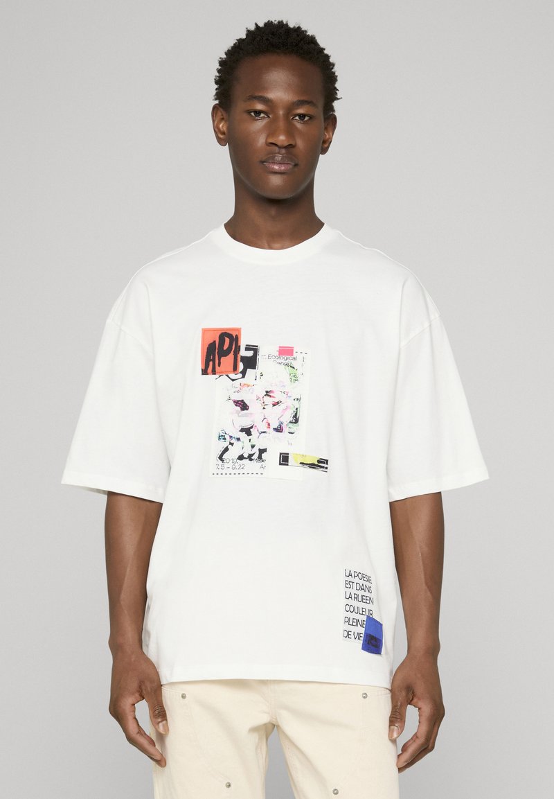 Hvid oversized T-shirt med farverigt grafisk print og tekstdetaljer. Blødt bomuldsmateriale, rund hals, korte ærmer.