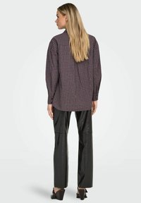 Camisa de manga larga a cuadros en púrpura oscuro y negro, combinada con pantalones de cuero sintético negro de talle alto. Textura suave, ajuste holgado.