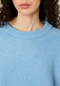 Ljusblå ulltröja med ribbad rund hals och mjuk textur, med en avslappnad passform och utan framträdande mönster eller detaljer.