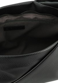 Das Innere der schwarzen Lederhandtasche verfügt über eine strukturierte Oberfläche, eine Reißverschlusstasche und ein glattes Futter mit einem subtilen Glanz.