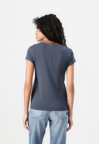 T-shirt de manga curta e decote redondo em algodão cinza escuro. A parte de trás apresenta uma textura suave com detalhamentos de costura mínimos. Estilo ajustado.