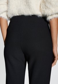 Schwarze hochtaillierte Hose mit einer glatten, elastischen Textur. Das Design besteht aus einem geraden Bein und minimalen Nähdetails am Taillenbund.