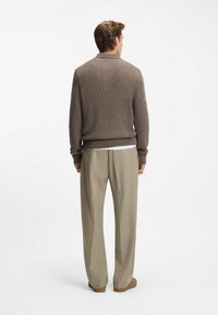 Bruine gebreide trui met een ribbeltextuur, ronde hals en lange mouwen, gecombineerd met lichtbeige op maat gemaakte broek en bruine schoenen.