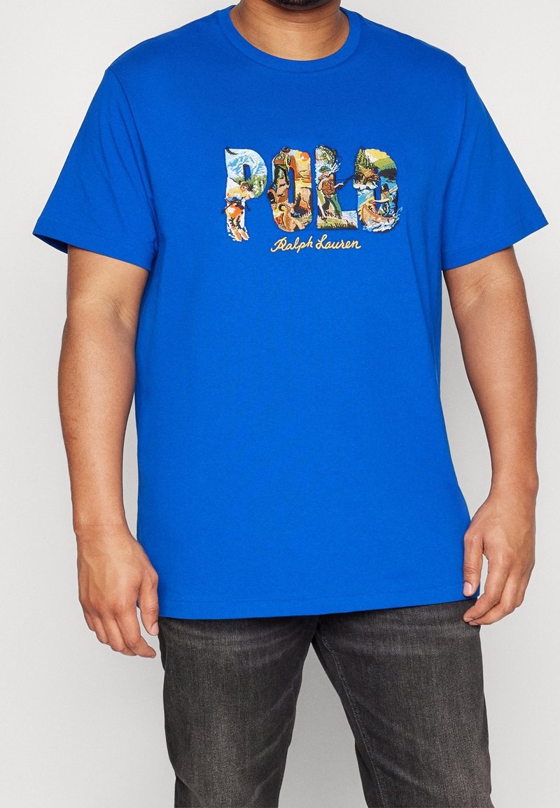 Blå bomullströja med en färgglad "Polo Ralph Lauren" grafisk design på framsidan, med korta ärmar och rundad halsringning.