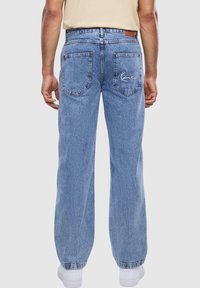 Light blue denim jeans with a relaxed fit, featuring a leather waistband patch and embroidered logo on the right back pocket.