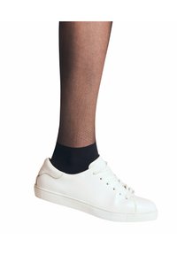 Witte leren sneakers met een ronde neus, platte zool en vetersluiting, gecombineerd met sheer zwarte kousen bij de enkel.