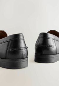 Scarpe in pelle nera con una texture liscia, design arrotondato e suole in gomma a basso profilo. Presentano cuciture decorative vicino alla parte posteriore.