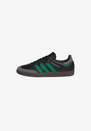 Black leather sneaker with green accents, featuring three stripes, textured gray toe cap, and black laces. Rubber sole with traction pattern.