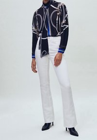 Czarna i biała bluzka w wzory z chustką na szyi, zestawiona z białymi spodniami dzwonami i czarnymi szpilkami z ostrym noskiem. Niebieskie akcenty na rękawach.