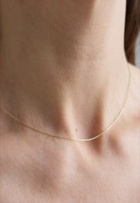 Colier din aur cu un design delicat și subțire. Are o textură netedă și strălucitoare și se așază ușor pe claviculă.