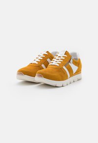 Yellow suede sneakers with white accents, rounded toe, and textured surface. Features laces and a decorative side zipper.