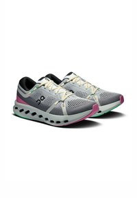 Grijze sportschoenen met een ademend bovenwerk van mesh, contrasterende zwarte en roze accenten, een gevoerde zool en zichtbare luchtzakken.