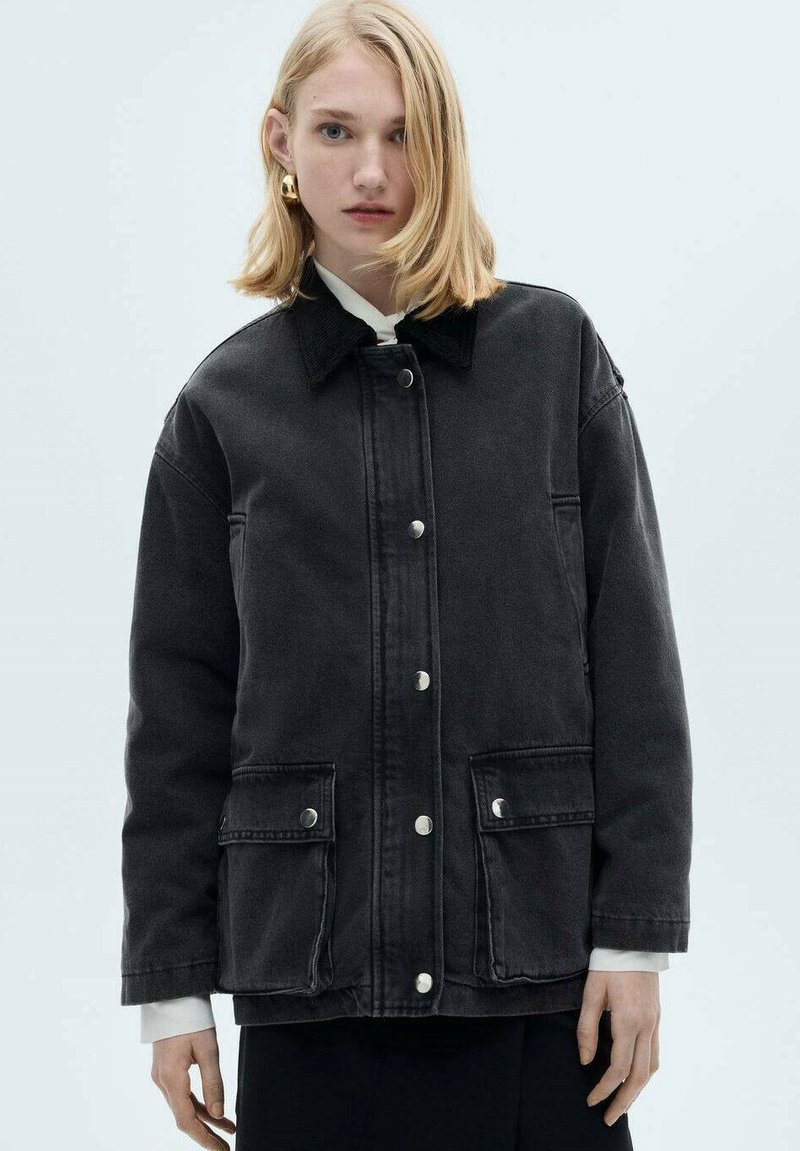 Black denim jacket with a collar, front snap closures, and two side pockets. Features a relaxed fit and visible stitching details.