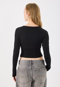 Top cropped negru cu maneci lungi, cu decolteu rotund. Asortat cu blugi gri cu talie înaltă, având buzunare pe spate și cusături vizibile.